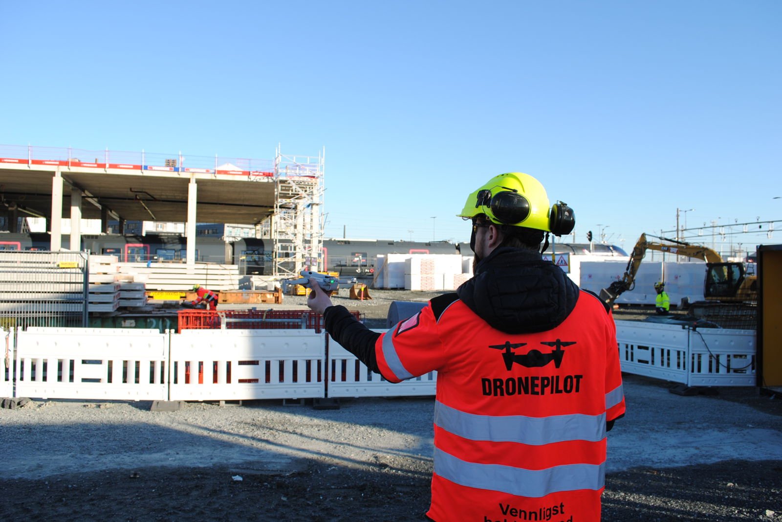 Dronepilot kledd i synlig vernetøy som kjører drone over byggeplassen